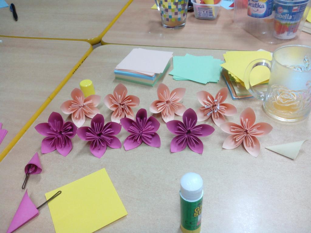 Różowe o pomarańczowe kwiaty  wykonane z papieru powkładane w 2 równoległe rzędy na stole