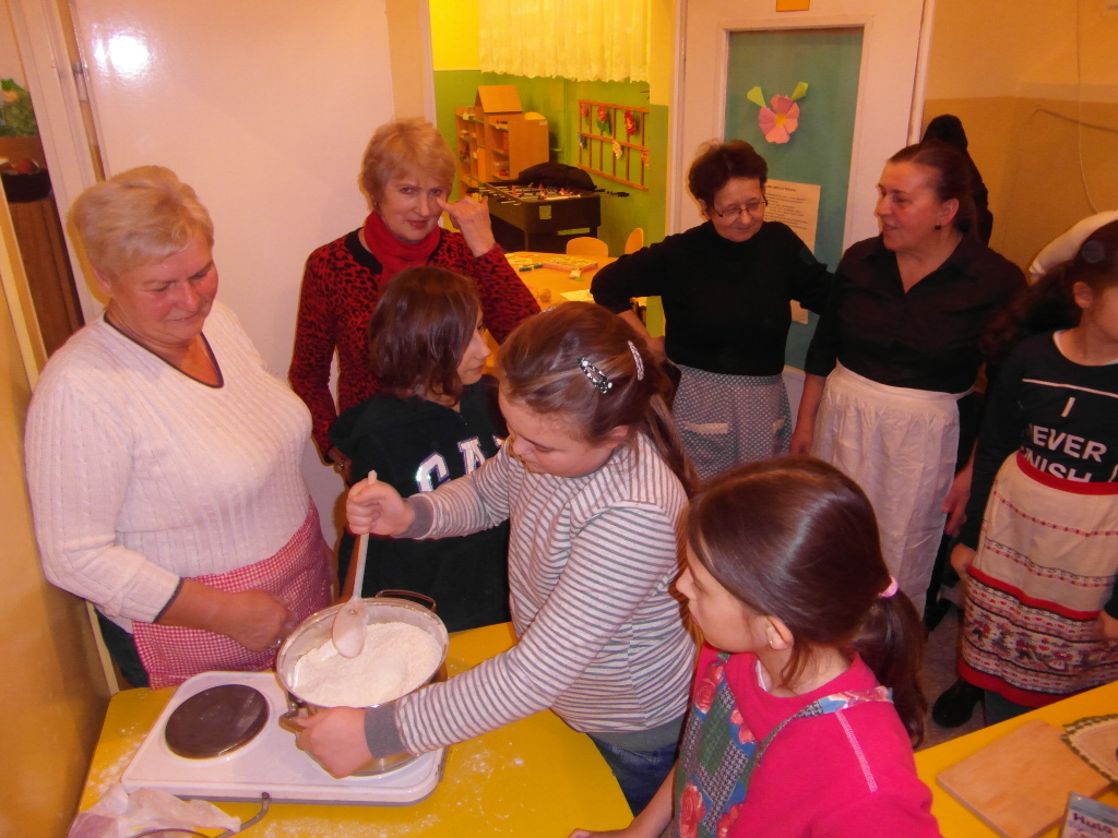 Zdjęcie przedstawia osoby dorosłe i dzieci podczas przygotowywania potrawy.