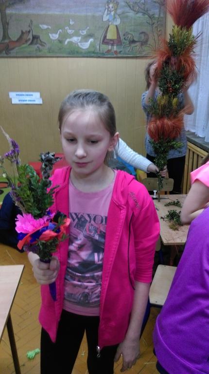 Dziewczynka w różowej bluzie prezentuje palmę wielkanocną